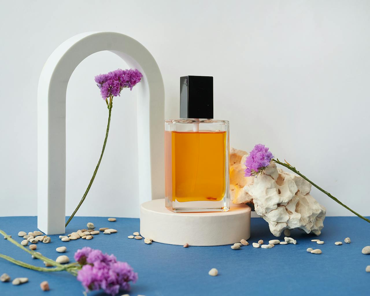 A contemporary perfume bottle displayed with purple flowers on a stylish pedestal.